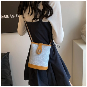 Detail of light blue denim bucket bag with brown trim and golden chain strap
