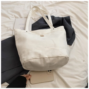 Detail shot of off-white canvas tote bag with metal emblem and smartphone for scale