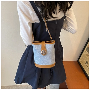 Rear view of a model wearing a blue denim bucket bag with brown leather trim and chain