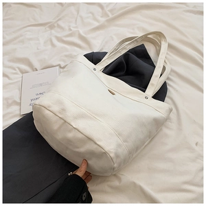 Detailed top view of a large cream canvas tote bag with metal rivets on white fabric