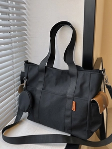 Large black nylon tote bag with side pocket and coin purse displayed by a window