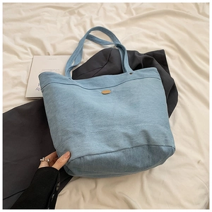 Close-up of light blue denim tote bag featuring a metallic oval badge and wide stitching