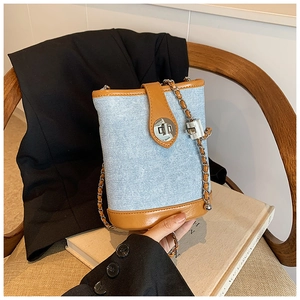Detail of light blue denim bucket bag with brown leather trim and silver chain on a chair