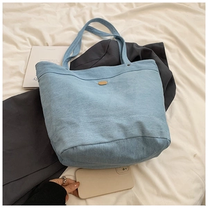 Detail of light blue denim tote bag featuring a minimalist gold oval metal plaque and handles