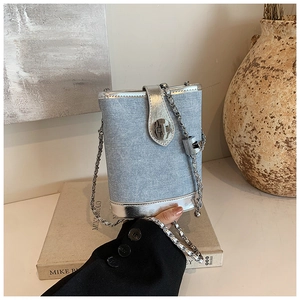Detail of light blue denim bucket bag with silver leather trim and metal chain strap