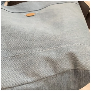 Detailed close-up of blue denim tote bag texture with precise white stitching and leather detail