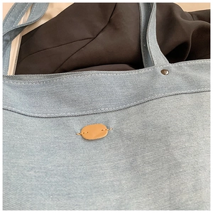 Close-up of blue denim tote bag texture showing neat stitching and leather brand tag