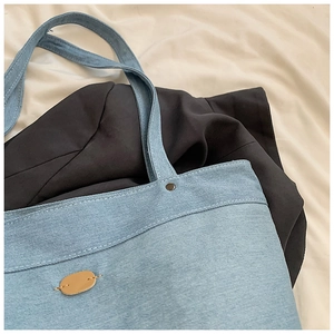 Close-up of light blue denim tote bag with brown leather patch and neat stitching detail