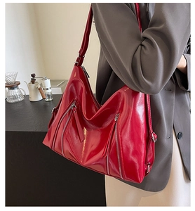 Detail of red glossy PU leather shoulder bag with decorative silver zippers on a model