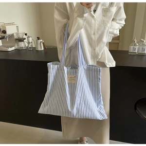 Blue and white striped canvas tote bag detail showing the logo label and shoulder strap