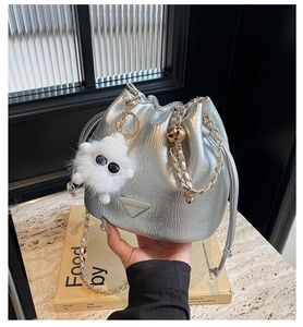 Close-up of silver chain bucket bag with plush charm and metallic triangle logo plate