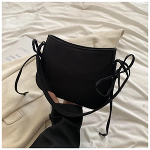 Détail du sac bandoulière en toile noire avec des nœuds décoratifs sur fond de tissu blanc