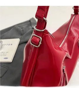 Detail of red patent PU leather bag showing adjustable shoulder strap with silver metal buckle
