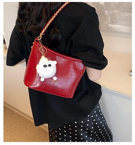 Detail of red leather shoulder bag featuring gold chain strap and teddy bear charm
