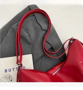 Detail of glossy red patent leather handbag with long straps and metal zipper design