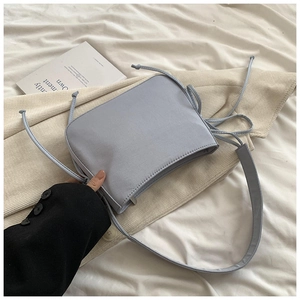 Détail du mini sac bandoulière bleu clair en toile avec cordons décoratifs sur le lit