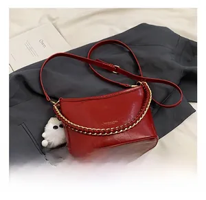 Detail of red faux leather handbag with gold chain handle and white plush charm