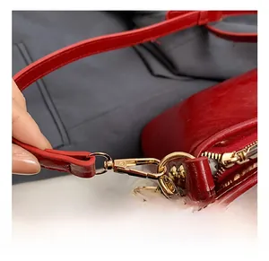 Close-up of golden metal swivel hooks and zipper on a glossy red leather bag detail