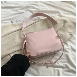 Détail du sac bandoulière rose clair avec nœud décoratif et large sangle sur fond de tissu