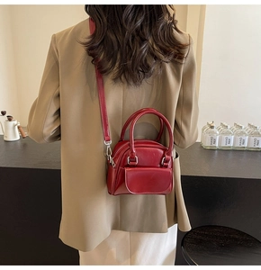 Detail of a burgundy leather satchel with double handles and a removable shoulder strap