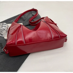 Detail of red glossy shoulder bag featuring symmetric silver zippers and modern trapezoid design