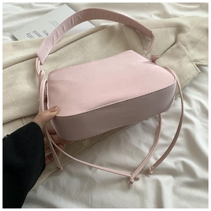 Gros plan sur le sac baguette rose avec cordons décoratifs et large bandoulière fixe