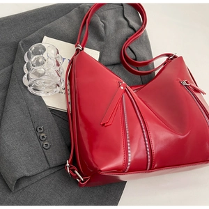 Detail of red glossy leather hobo bag with silver zipper accents on grey suit