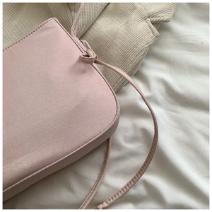 Gros plan du sac en tissu rose avec bandoulière nouée sur un fond doux et texturé
