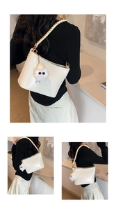 Detail view of off-white bucket bag with gold chain strap and plush monster charm