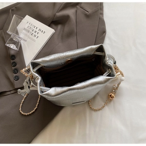 Macro shot of silver metallic bucket bag with drawstring closure and golden chain detail