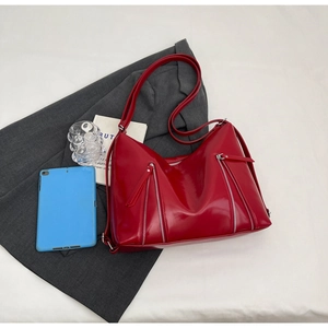 Detail of red glossy patent leather shoulder bag with decorative metallic zippers