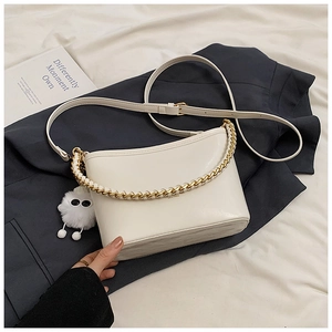 Detailed shot of cream leather handbag with gold chain strap and plush monster charm
