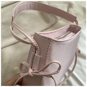 Détail d'un sac à bandoulière rose avec nœud latéral et fermeture éclair en métal