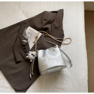 Close-up of metallic silver bucket bag with gold chain strap and plush charm