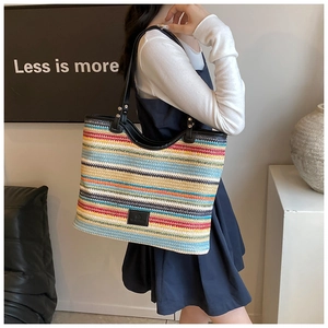 Close-up of rainbow woven tote bag with black leather handle and metal rivet details
