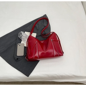 Detail of red glossy tote bag with dual silver zippers and a long shoulder strap