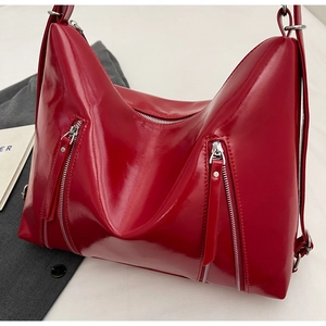 Close-up of vibrant red glossy leather bag with silver zipper detail and adjustable strap