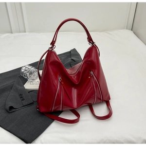Close-up of red patent leather tote bag with silver dual zippers on white fabric background