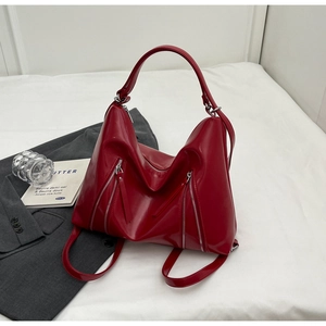 Close-up of a glossy red bow tote bag with metallic zippers on a stylish grey blazer backdrop