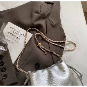 Detail of silver chain bag featuring pleated texture and golden adjustment ball