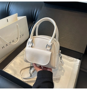 Detail of a creamy white mini crossbody bag featuring silver hardware inside a gift box