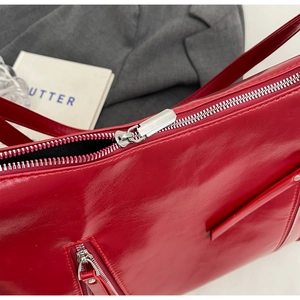 Detail of red glossy patent leather bag with oversized silver metal zipper and sleek texture