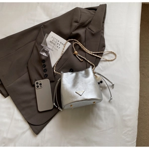 Detail of silver bucket bag with drawstring closure, metal feet and chain strap