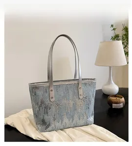 Detail of a large silver sequin tote bag with sleek leather handles on a white desk