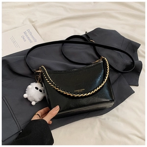 Detail of black faux leather bag with gold chain strap and decorative white fur pompom