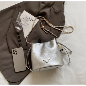 Detail of silver metallic bucket bag featuring chain strap and plush ball accessory