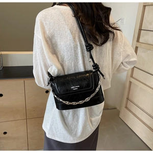 Detail of black crossbody bucket bag with silver chain and knotted strap on model