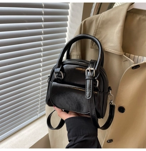 Close-up of black glossy mini crossbody bag with round handle and flap detail