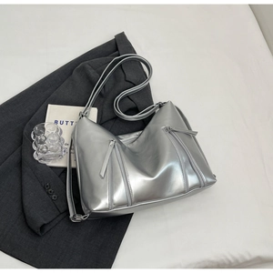 Detail of silver metallic tote bag with triple zipper design on a grey blazer suit