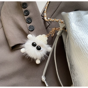 Close-up of a white plush monster charm with big eyes hanging on a silver chain bag